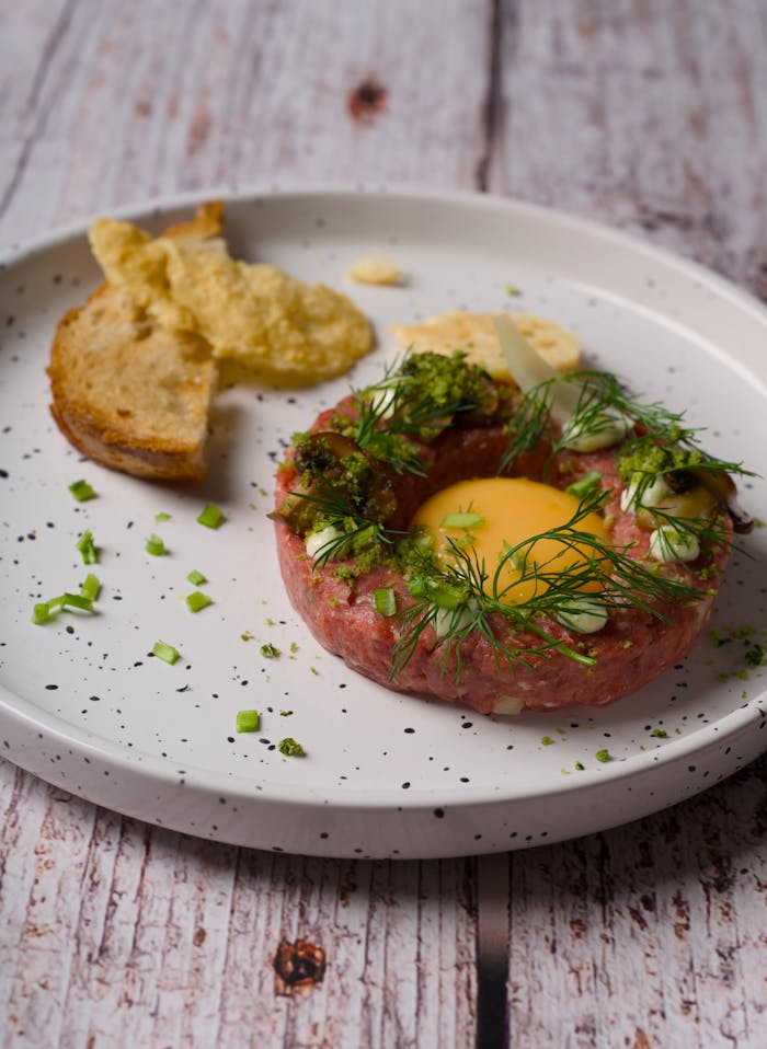 Elegant beef tartare garnished with quail egg and herbs served in a rustic setting.